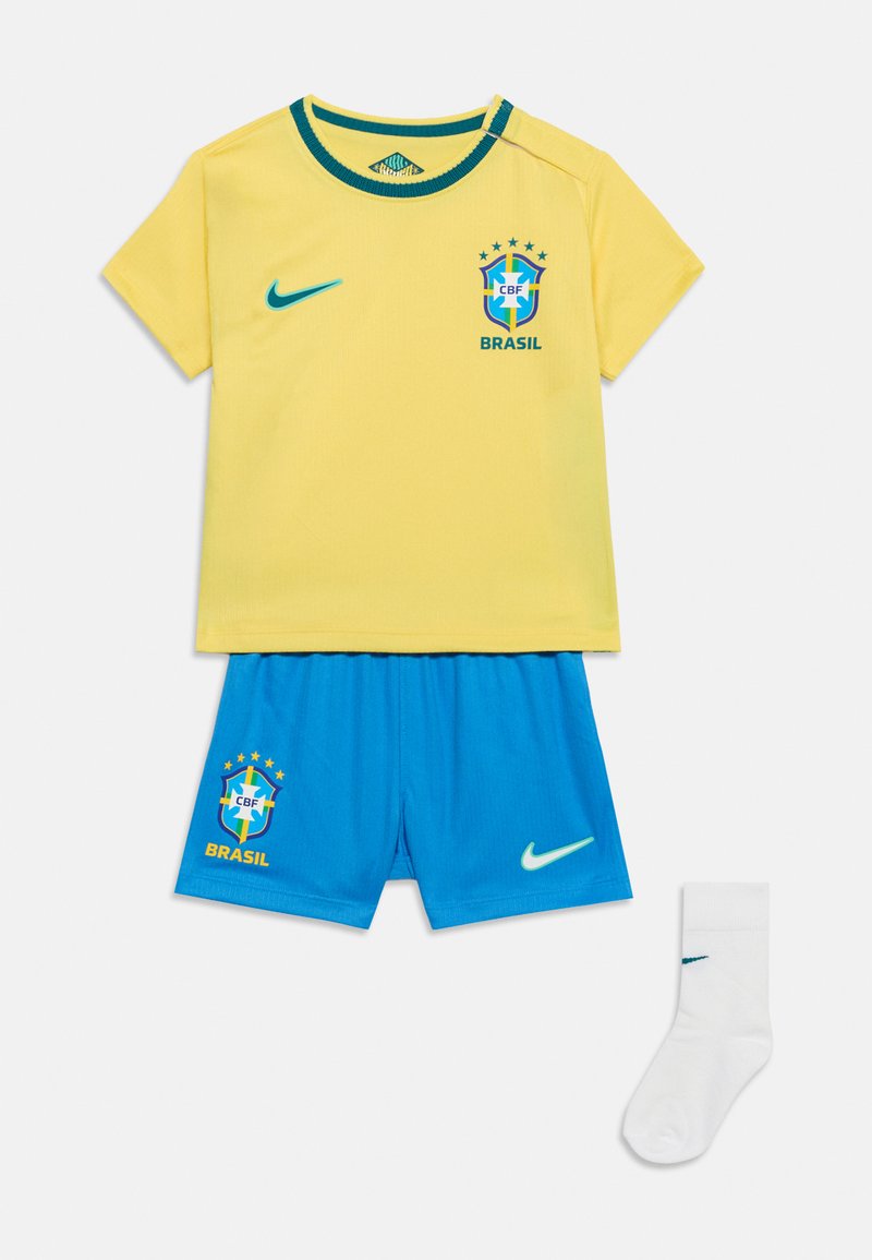 Κίτρινη φανέλα ποδοσφαίρου της Βραζιλίας με μπλε λογότυπο Nike, μπλε σορτς με έμβλημα της Βραζιλίας και λευκά καλτσάκια με το λογότυπο Nike, τοποθετημένα επίπεδα σε λευκό φόντο.