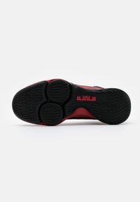 Sportssko sål med en sort tekstureret gummibase med røde detaljer, rund hæl og cirkulære mønstre.