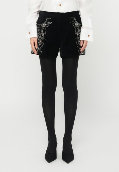 Black velvet shorts featuring intricate floral and leaf embroidery on the front pockets, worn with black tights and pointed-toe heels.