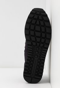 Semelle noire de basket avec motif géométrique affichée verticalement sur fond blanc anguleux.