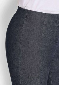 Donkergrijze denim broeken met een hoge taille, een gladde textuur en discrete stiksels langs de naden. Close-up van de stof en de vorm.