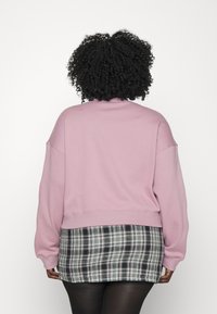 Rosa oversized sweatshirt med sänkta axlar, i kombination med en svart och vit rutmönstrad minikjol. Mjuk textur, kort design och avslappnad passform.