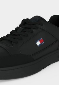 Baskets noires Tommy Jeans avec laçage à l'avant, semelle basse et écusson logo rouge, blanc et bleu sur le panneau latéral.