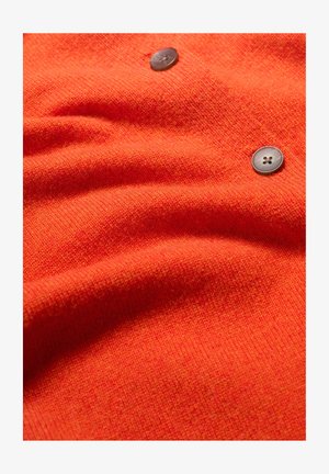 Tejido de punto naranja con una textura suave, que presenta dos botones oscuros con un diseño de cuatro agujeros, creando un sutil interés visual.