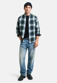 Grön och blå rutig skjorta ovanpå en svart kabelstickad tröja, tillsammans med ljusblå jeans och svarta slip-on stövlar.