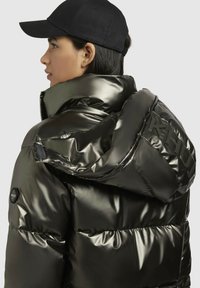 Zwarte pufferjack met glanzende, metallic afwerking, oversized capuchon en zijzakken met rits. Bevat een zwarte pet met gebogen visor.
