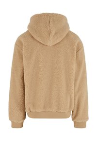 Tan fleece hettegenser med en teksturert, fluffy overflate. Har hette og ribbestrikkede mansjetter langs kanten og ermene. Minimalistisk design.