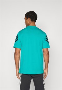 Turkis bomulds t-shirt med korte ærmer, har tre sorte striber på hver skulder. Lige hæm og rund halsudskæring.