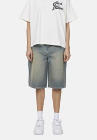 Shorts in denim azzurro chiaro con un effetto scolorito, presentano una vestibilità comoda. Abbinati a una t-shirt bianca con grafica e sneakers bianche.