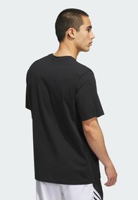 Camiseta de algodón negra con mangas cortas, corte relajado, escote redondo y textura suave, vista desde la parte posterior.