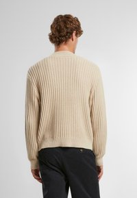 Cardigan bej tricotat, cu textură striată, gât rotund și manșete ajustate. Confectionat dintr-un material moale, are o croială lejeră și un tiv subtil.