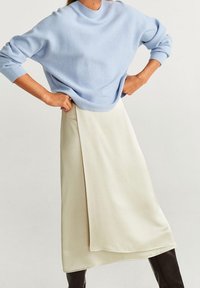 Suéter oversize azul claro con puños anchos, combinado con una falda asimétrica color crema. La tela parece suave y lisa.