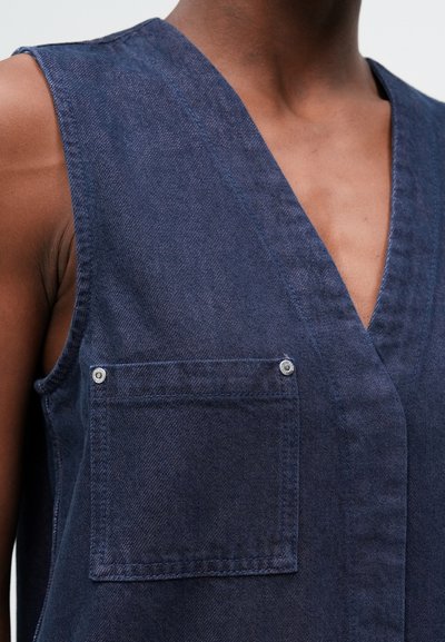 Mornarsko modra denim majica z V-izrezom, brez rokavov in žepom na prsih s pritrdilnim gumbom. Gladka tekstura in čisti šivi.