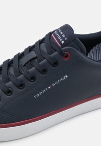 Granatowe skórzane tenisówki z okrągłym noskiem, białą podeszwą, czerwonymi akcentami i detalem logo. Posiadają sześć otworów na sznurowadła z szarymi sznurowadłami i teksturowane wykończenie wnętrza.