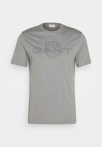 T-shirt en coton gris avec un col rond, des manches courtes, et un graphique bleu marine représentant un bouclier avec des étoiles et le mot "GAINT".