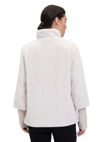 Kurtka z futra syntetycznego w jasnoróżowym kolorze, z wysokim kołnierzem, opadającymi ramionami oraz akcentami na rękawach w postaci prążkowanego dzianiny. Gładka, miękka faktura.