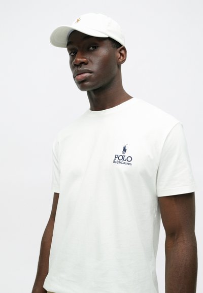 Λευκό βαμβακερό T-shirt με κοντά μανίκια, που διακοσμείται με ένα μικρό μπλε λογότυπο "Polo Ralph Lauren" στο στήθος. Συνδυασμένο με ένα λευκό καπέλο.