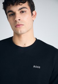 Svart, strukturert crewneck t-skjorte med et brodert "BOSS"-logo på venstre bryst, laget av bomull eller et lignende mykt stoff.