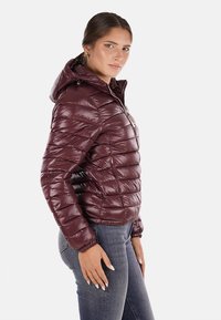 Giacca puffer borgogna con un design attillato, trapuntatura orizzontale, cappuccio staccabile e tasche con zip. Il materiale ha una consistenza lucida e liscia.
