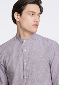Camicia button-up grigio chiaro con colletto alla coreana, realizzata in tessuto testurizzato. Presenta una tasca sul petto e bottoni bianchi.