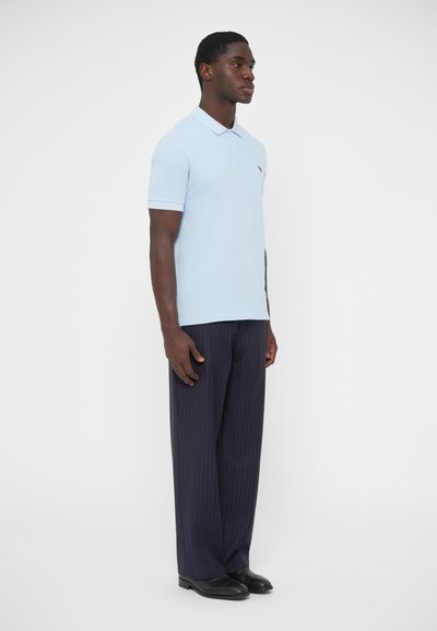 Ανοιχτό μπλε πόλο μπλουζάκι με κοντά μανίκια και γιακά, σε συνδυασμό με σκούρο παντελόνι με λεπτές ρ�ίγες και μαύρα παπούτσια. Απλός σχεδιασμός, χωρίς σχέδια.