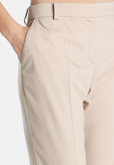 Pantalons beige ajustés avec une texture lisse, dotés de poches latérales et d'un design épuré. Tissu léger adapté à diverses occasions.