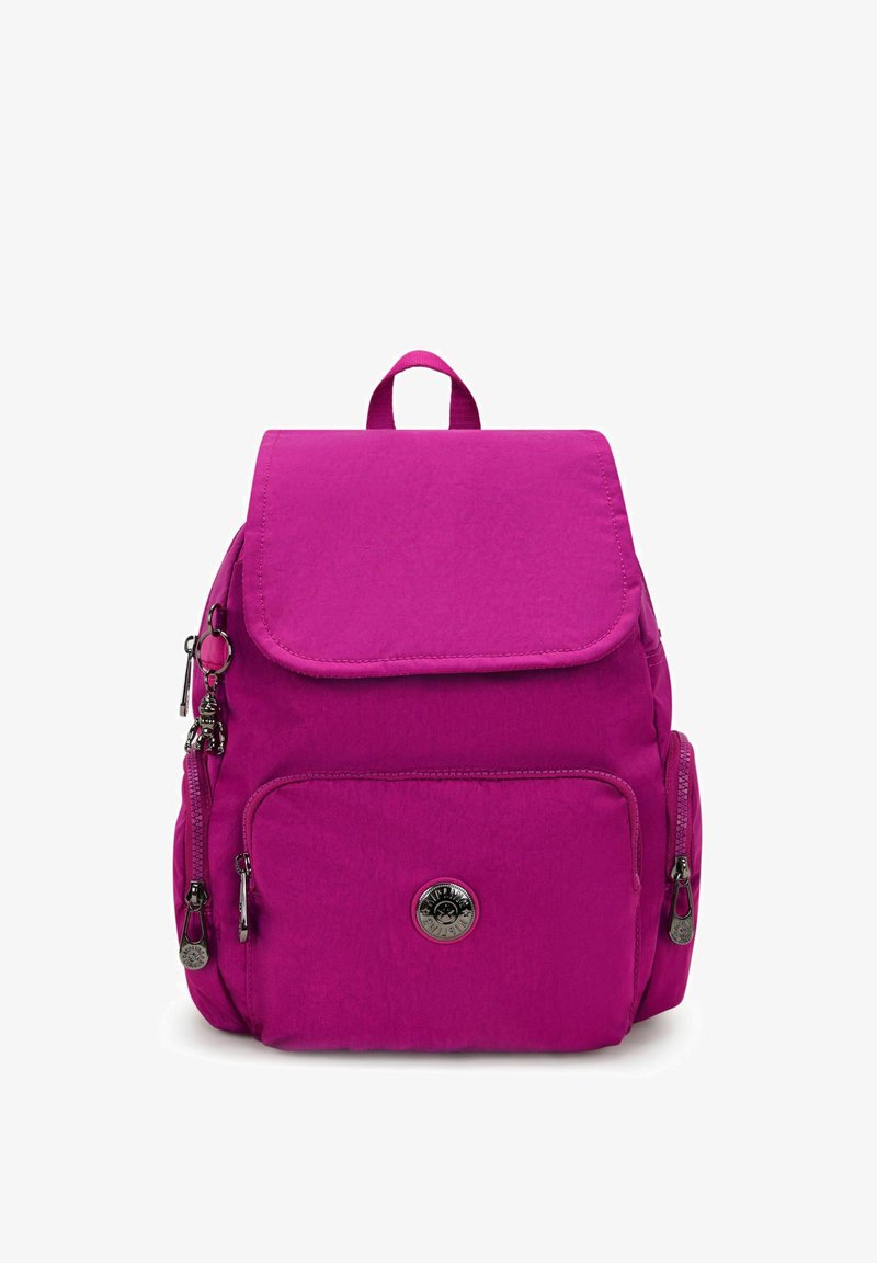 Sac à dos magenta avec une fermeture à rabat, comportant plusieurs poches zippées, une texture lisse, une poignée supérieure et un charm décoratif sur la fermeture éclair.