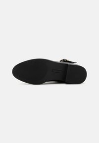 Semelle de chaussure noire avec une forme plate et arrondie. Présente un caoutchouc texturé pour l'adhérence et une surface lisse. Les accents comprennent un design minimaliste.