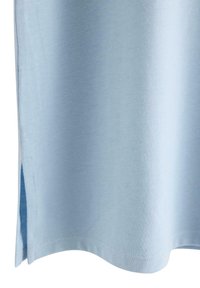 Hellblaues Baumwoll-T-Shirt mit glatter Textur, ausgestattet mit einem abgerundeten Saum und seitlichen Schlitzen für mehr Bewegungsfreiheit. Einfaches und sauberes Design.