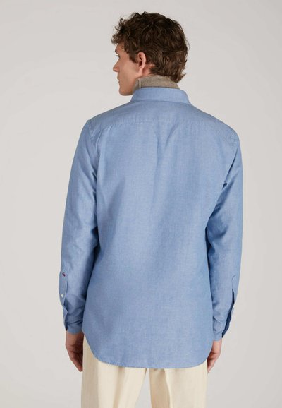 Camicia button-up azzurra chiara con maniche lunghe, colletto, pieghe sul retro e orlo arrotondato. Presenta un colletto interno in contrasto di color beige chiaro.