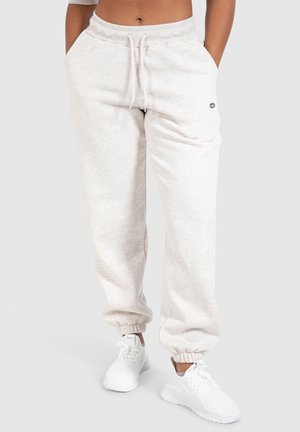 Person trägt hellgraue Jogginghose mit Kordelzug in der Taille und elastischen Bündchen, kombiniert mit weißen Sportschuhen vor neutralem Hintergrund.