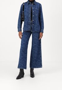 Jeansowa kurtka i szerokie spodnie w ciemnoniebieskim kolorze z kwiecistym wzorem. Posiada metalowe guziki, kieszeń na piersi oraz luźny krój. Czarne botki na obcasie.
