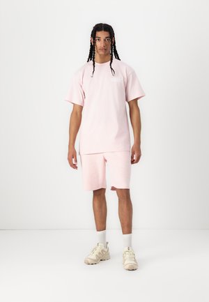 Camiseta de algodón de color rosa claro y pantalones cortos a juego, con un corte holgado y un diseño sencillo. Combinado con zapatillas de color claro y calcetines blancos.