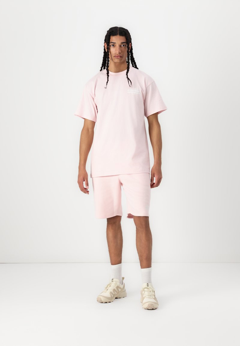 Helles rosa Baumwoll-T-Shirt und passende Shorts, mit lockerer Passform und schlichtem Design. Kombiniert mit hellen Sneakern und weißen Socken.