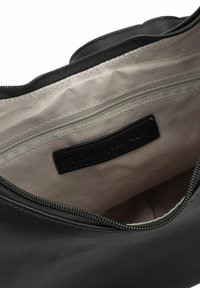Schwarze Lederhandtasche mit einem Reißverschluss, ausgestattet mit einer glatten Oberfläche, beiger Innenausstattung und einer Innentasche mit silbernem Reißverschluss.