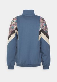 Felpa blu con colletto alto, pannelli neri e beige a contrasto e accenti a motivo floreale colorato sulle spalle.