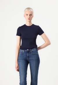 T-shirt fitted bleu marine en coton, avec un col rond et des manches courtes, associé à un jean en denim bleu clair.