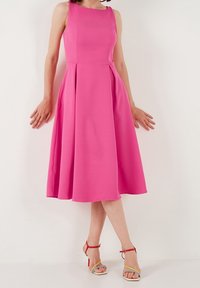 Robe sans manches fuchsia avec un corsage ajusté, une jupe plissée et une longueur au genou. Assortie à des sandales à lanières multicolores.