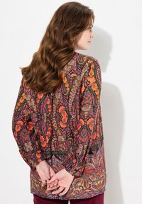 Multicolored long-sleeve blouse featuring a floral and paisley pattern in shades of orange, pink, and black. Fitted cuffs and loose design.