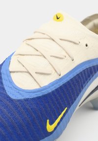 Blue and white athletic shoe featuring textured fabric, cream laces, and a small yellow logo. Streamlined design with a curved shape.