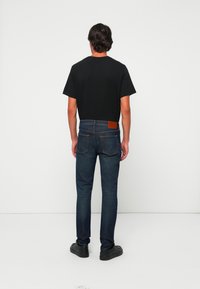 Čierne bavlnené tričko v kombinácii s tmavými džínsy s koženou nášivkou v oblasti pásu a slim fit strihom, doplnené čiernymi topánkami.
