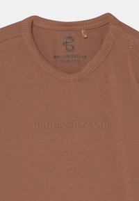 Camisa castanha de manga curta feita de tecido macio. Apresenta um decote arredondado com botões de pressão e a marca "BRUUNS BAZAAR" em relevo. Tamanho 80 cm.
