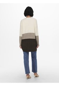 Neulejakku, jossa on kolme väriblokkia: kermanväri, taupe ja tummanvihreä. Pitkät hihat, rento istuvuus ja keskipitkä malli. Pehmeä pinta.