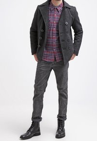 Černý vlněný kabát s dvouřadými knoflíky, červená a modrá kostkovaná košile, šedé džínové kalhoty a černé šněrovací boty.
