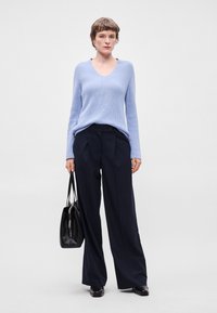 Ανοιχτό μπλε πουλόβερ με v λαιμόκοψη, ριγωτή υφή. Μαύρο παντελόνι σε φαρδιά γραμμή με λεπτές ρίγες. Μαύρη τσάντα με λουρί, φορεμένη στον ώμο. Απλός σχεδιασμός.