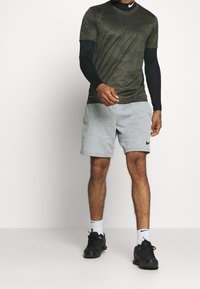 Šedé sportovní šortky Nike s elastickým pasem, zkombinované s tmavě zeleným, texturovaným, krátkým sportovním trikem. Černé sportovní boty.