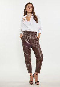 Bruine faux leren broeken met een hoge elastische tailleband en zijzakken, gecombineerd met een witte blouse en zwarte hakken.