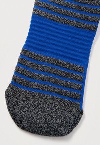 Δάχτυλο πλεκτής κάλτσας σε μαύρο και γκρι ανάμεικτο νήμα με οριζόντιες ρίγες σε μπλε και μαύρο πάνω σε μπλε ριμπ ύφασμα.