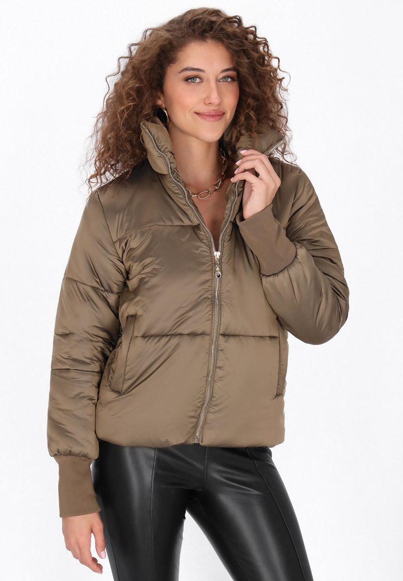 Brązowa kurtka puchowa z wysokim kołnierzem i zapięciem na zamek, z prążkowanymi mankietami i krótkim fasonem. Gładka, świecąca tekstura i pikowane sekcje.