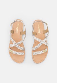 Sandales en cuir marron avec des brides blanches tressées, design ouvert sur le devant, présentant un accent doré sur le côté et une semelle plate.